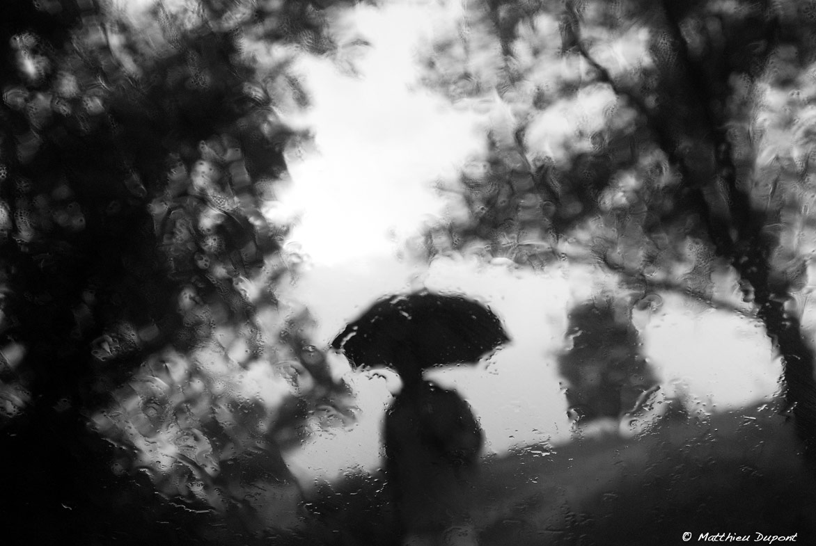 vue depuis une fenêtre humide, une silhouette sous un parapluie s'approche. Photo Matthieu Dupont