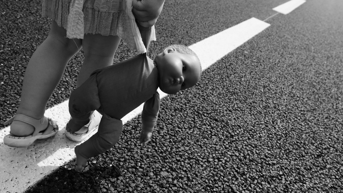 Une petite fille marche sur les bandes blanches d'une route, sa poupée à la main - Image noir et blanc de Matthieu Dupont