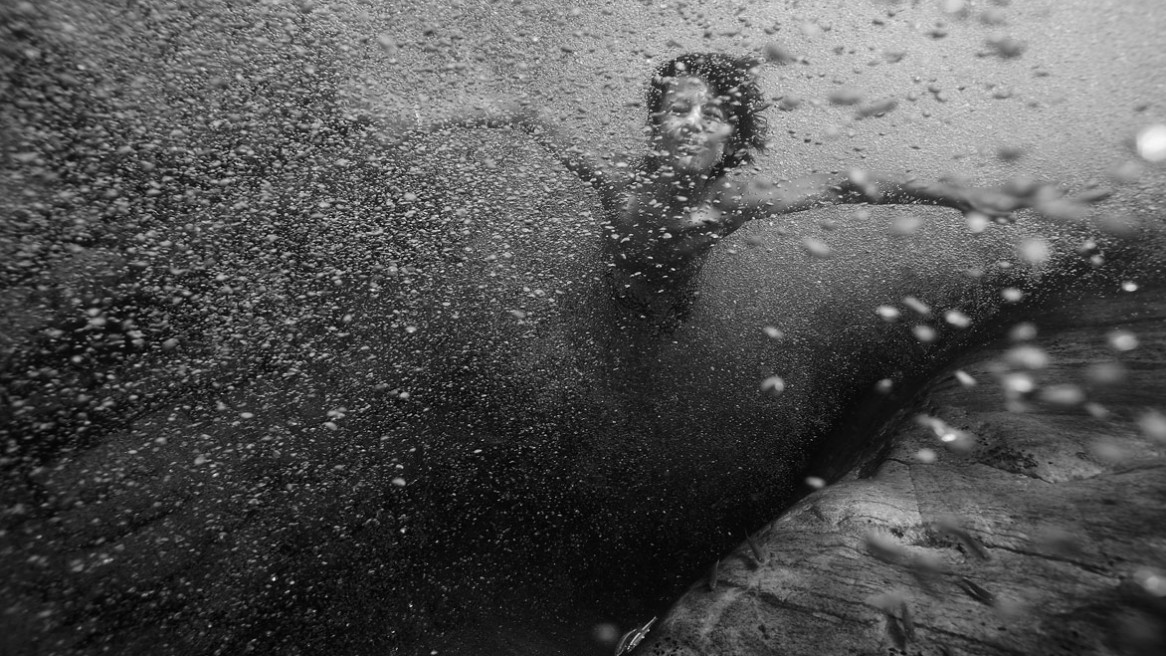 Un enfant sous l'eau nageant au milieu des bulles d'aire. Photo en noir et blanc de Matthieu Dupont