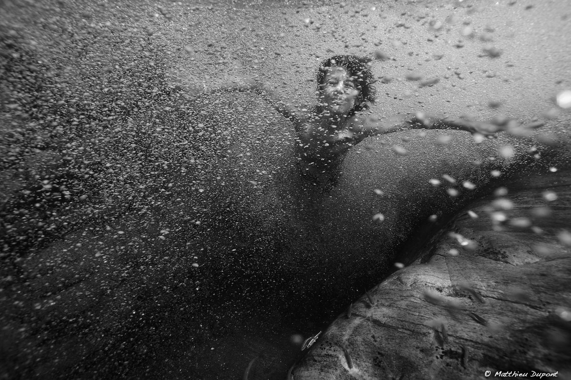 Un enfant sous l'eau nageant au milieu des bulles d'aire. Photo en noir et blanc de Matthieu Dupont