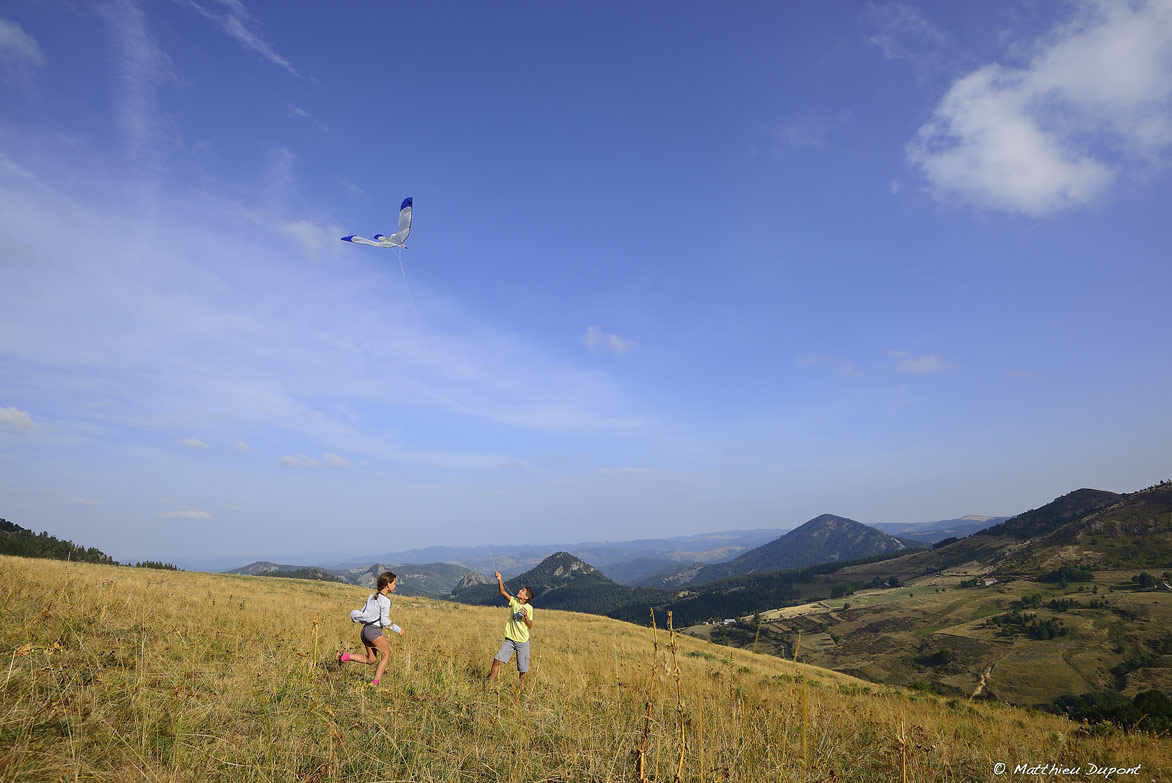 Deux enfants jouent avec un cerf-volant en Ardèche. Au loin les sucs et volcans d'Ardèche. Une photo de Matthieu Dupont