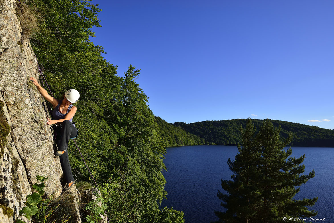 Jeune femme grimpant l'une des parois du site d'escalade du Lac d'Issarlès en Ardèche. Une photo de Matthieu Dupont