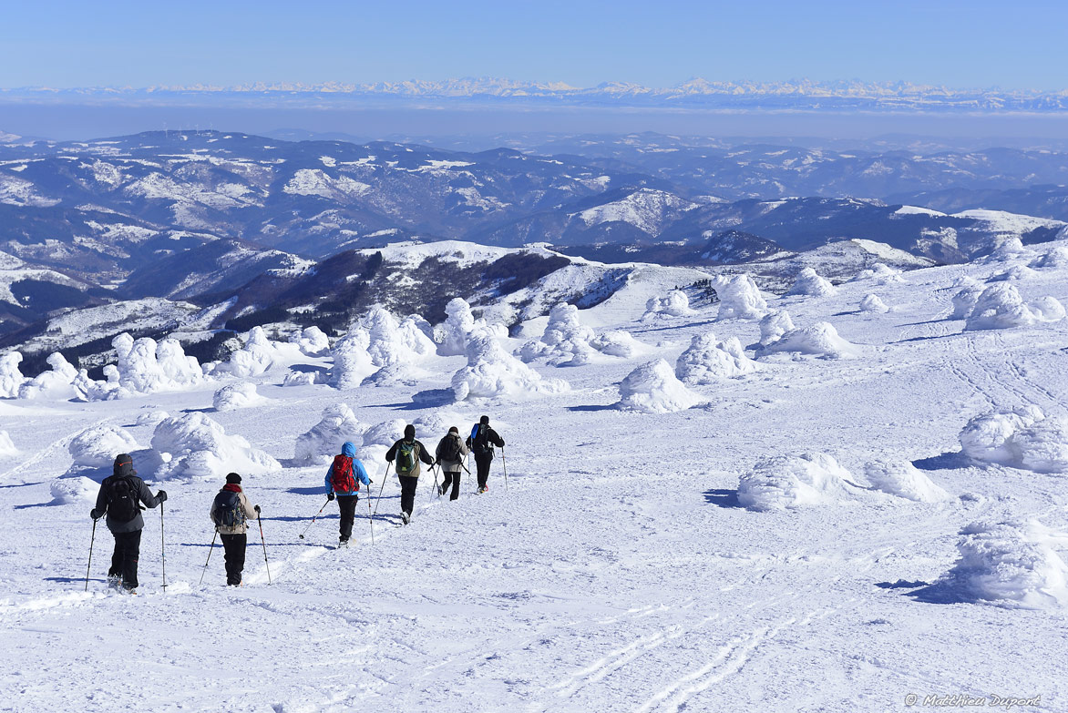 Groupe de promeneurs en raquette sur la neige du Mont Mézenc (Ardèche), avec un superbe panorama sur la Montagne ardéchoise, le Vercors et les Alpes. Photo Matthieu Dupont